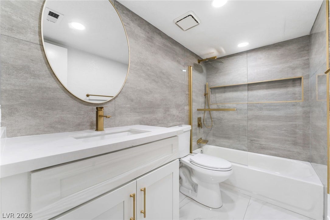 1017 Falconhead Lane, #102, Las Vegas, NV 89128 Elegant gold hardware accents contrast beautifully with textured gray wall tiles in this bathroom.