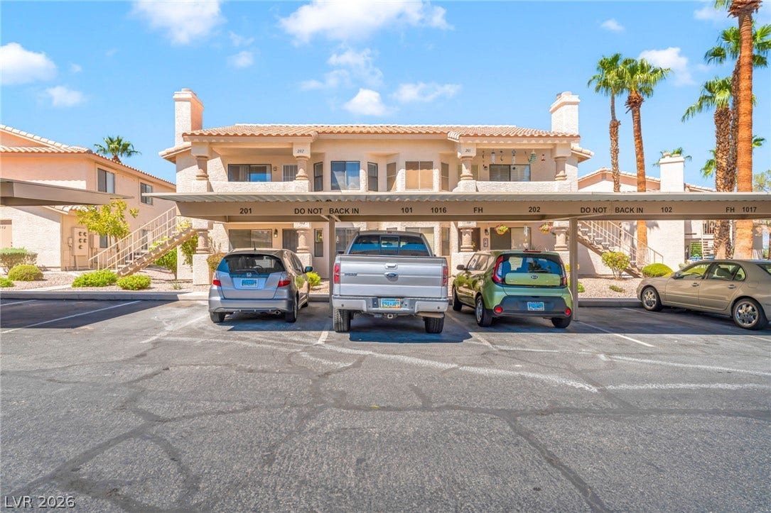 1017 Falconhead Lane, #102, Las Vegas, NV 89128 Covered parking structures sit directly in front of the stucco multi-level residential buildings.