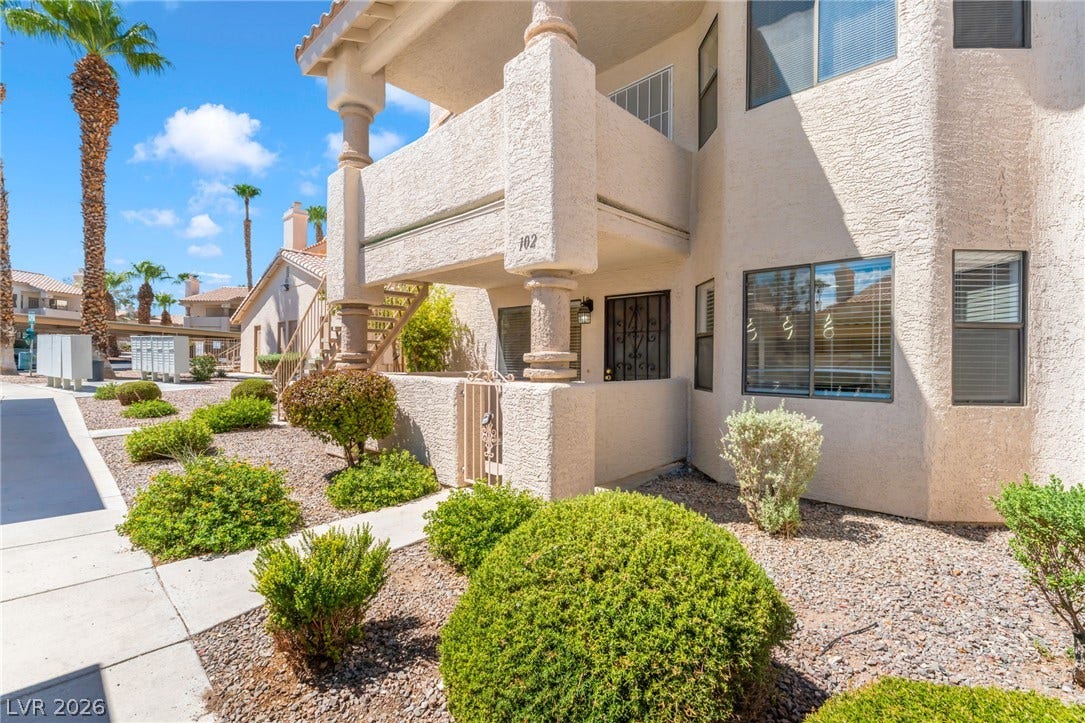 1017 Falconhead Lane, #102, Las Vegas, NV 89128 Desert landscaping and concrete walkways lead to a covered ground-floor entry under a stucco facade.