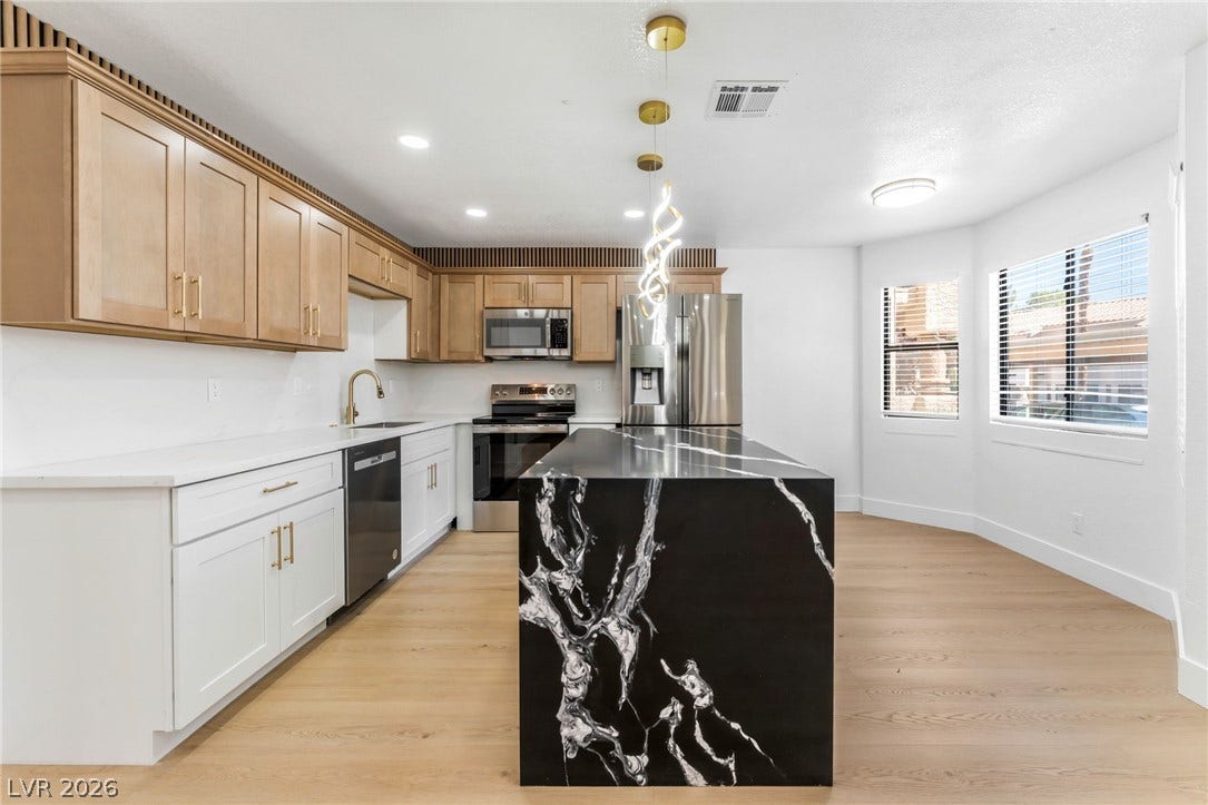1017 Falconhead Lane, #102, Las Vegas, NV 89128 Dramatic dark stone countertops pair with warm wood cabinetry and light hardwood flooring.