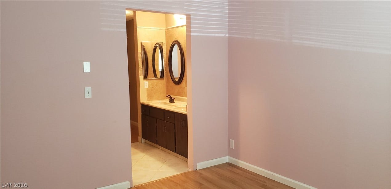An open doorway connects the wood-floored bedroom directly to an attached bathroom vanity area.