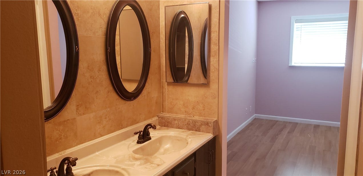 A classic double vanity with stone tile walls connects seamlessly to an adjacent space.