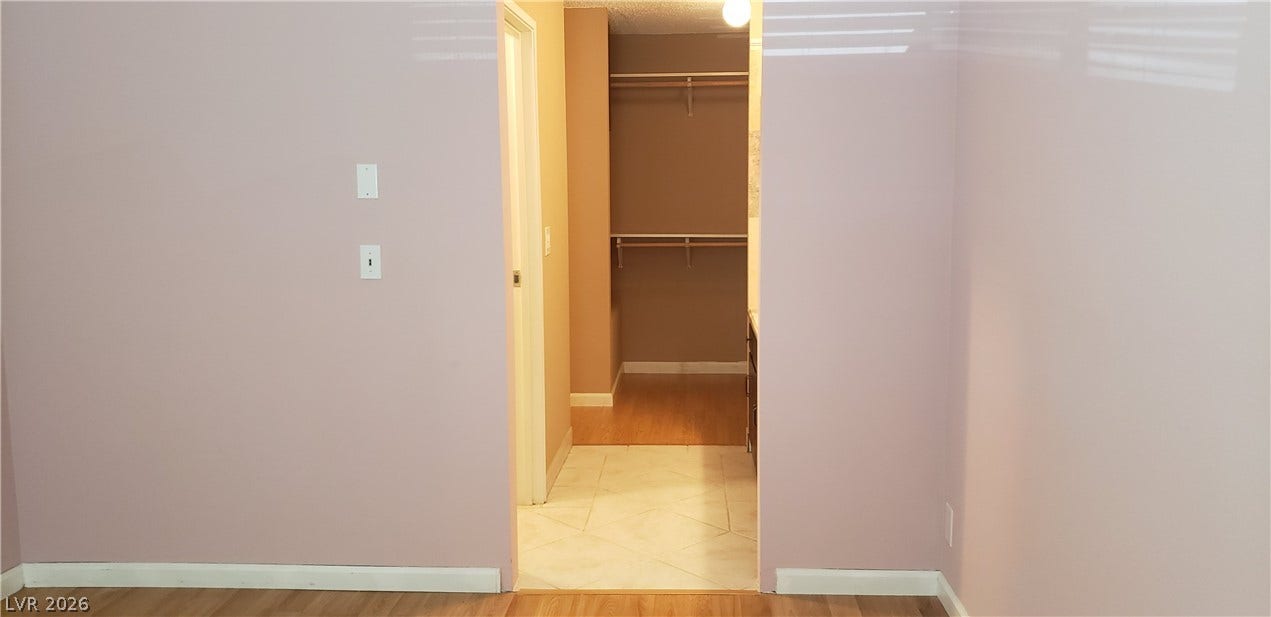 Smooth wood-style flooring transitions into a tile hallway leading to a spacious walk-in closet.