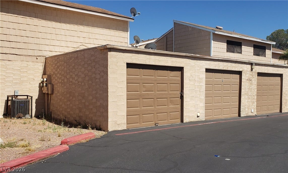 Detached garage units with classic roll-up doors stand adjacent to the paved driveway.