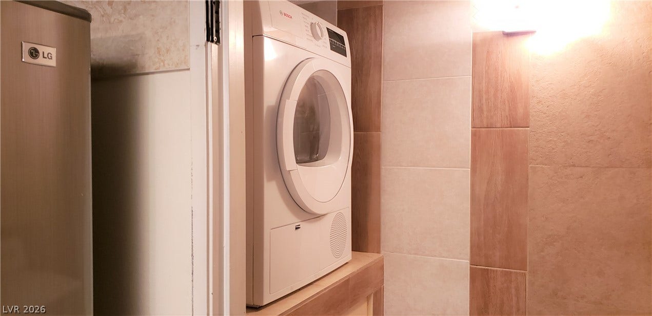 A dedicated laundry nook features textured wall tile and integrated appliances.