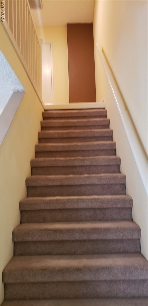 Carpeted stairs ascend to a bright upper landing with secure handrails and railings.