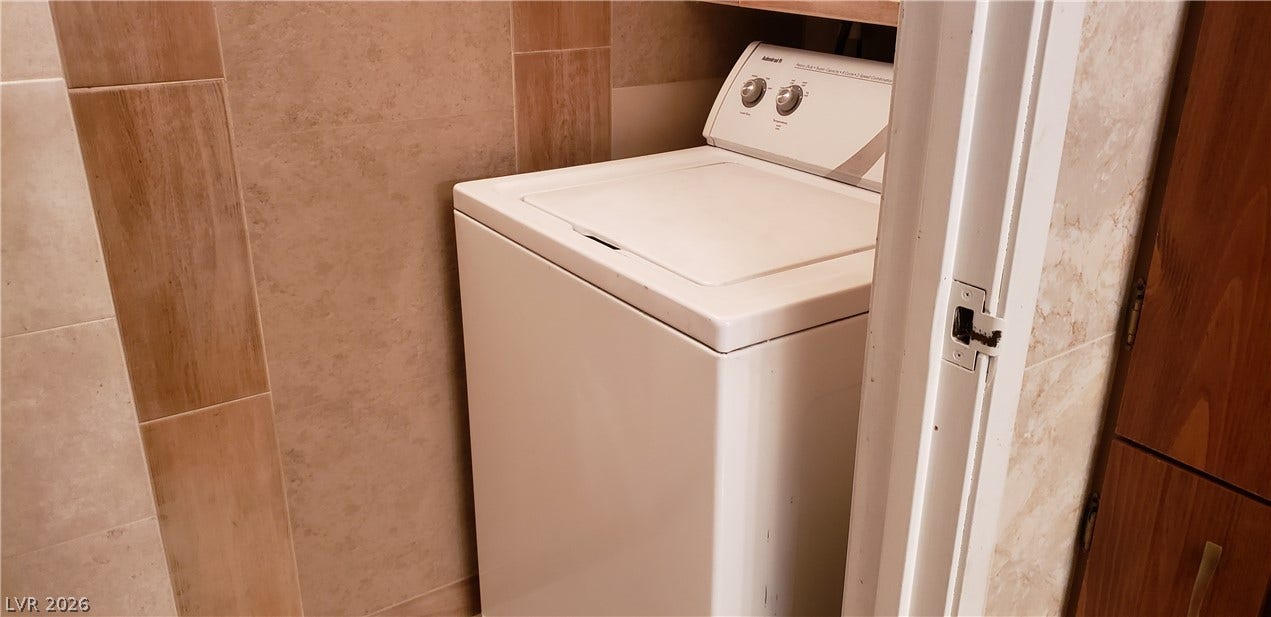 Tiled walls frame this dedicated utility space featuring a convenient top-loading washing machine.