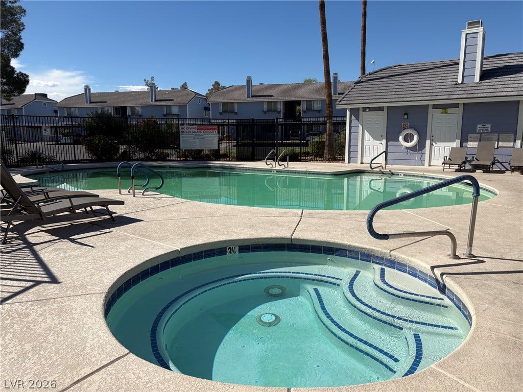 A sparkling community pool and spa area is surrounded by concrete decking and tall palms.