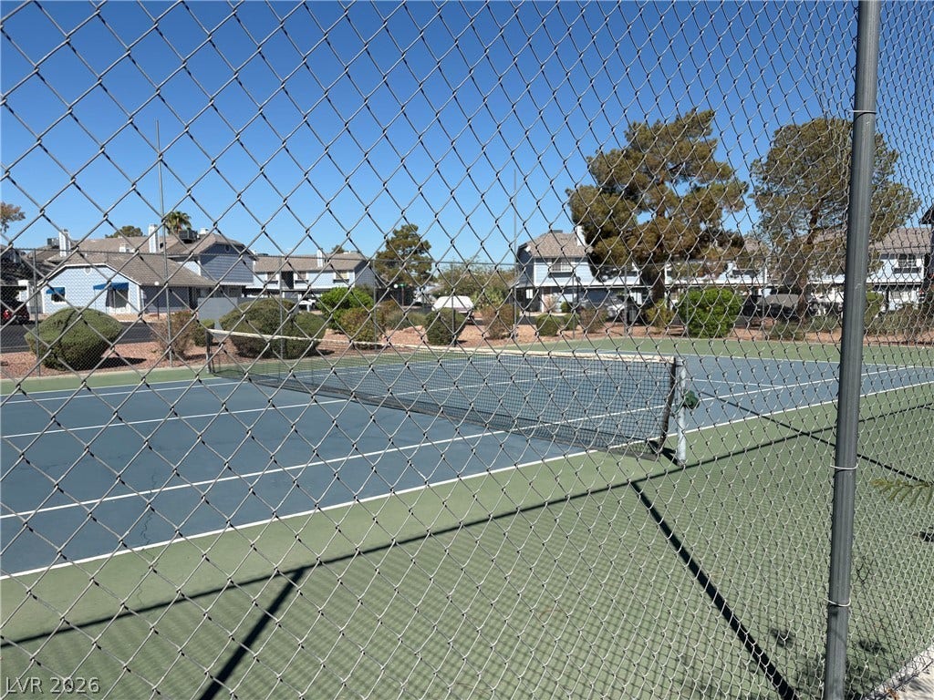 An outdoor tennis court is enclosed by chain-link fencing under clear blue skies.