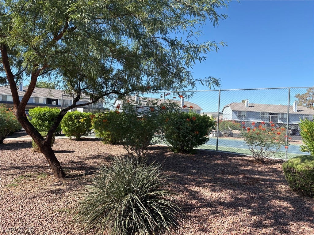 Lush landscaping and desert plantings surround a fenced neighborhood recreational facility under clear blue skies.