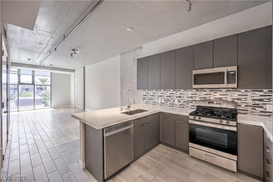 353 E Bonneville Avenue, #754, Las Vegas, NV 89101 Sleek Modern Kitchen features Quartz Countertops, Decorative Tile Backslash, Breakfast Bar, Stainless-Steel Gas Range, Dishwasher, and Microwave