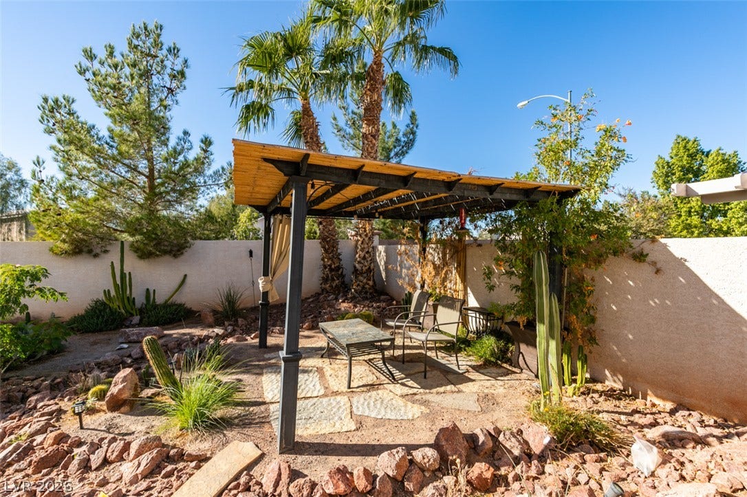 A shaded pergola offers a peaceful retreat amidst desert landscaping and mature palm trees.