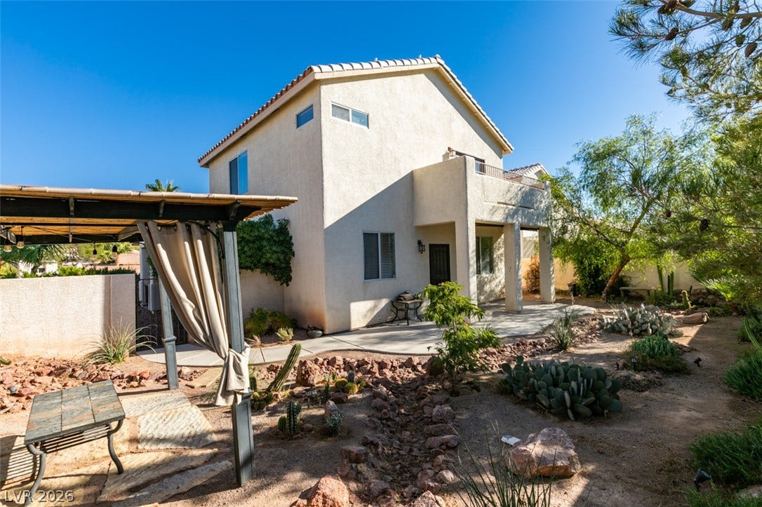 Arid landscaping surrounds this multi-level home featuring a covered patio and upper-level balcony.