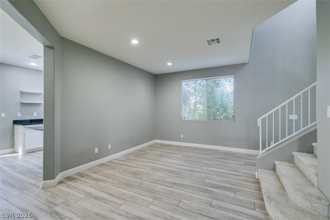 An open living space transitions seamlessly past a carpeted staircase under high ceilings.