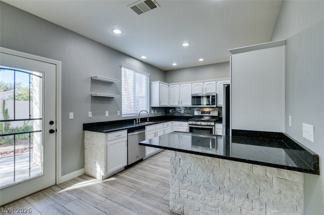 Polished granite countertops and stone accents highlight this contemporary kitchen with wood-look tile flooring.