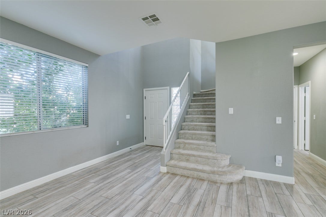 An open entryway showcases light-toned wood-look flooring and a carpeted staircase leading upward.