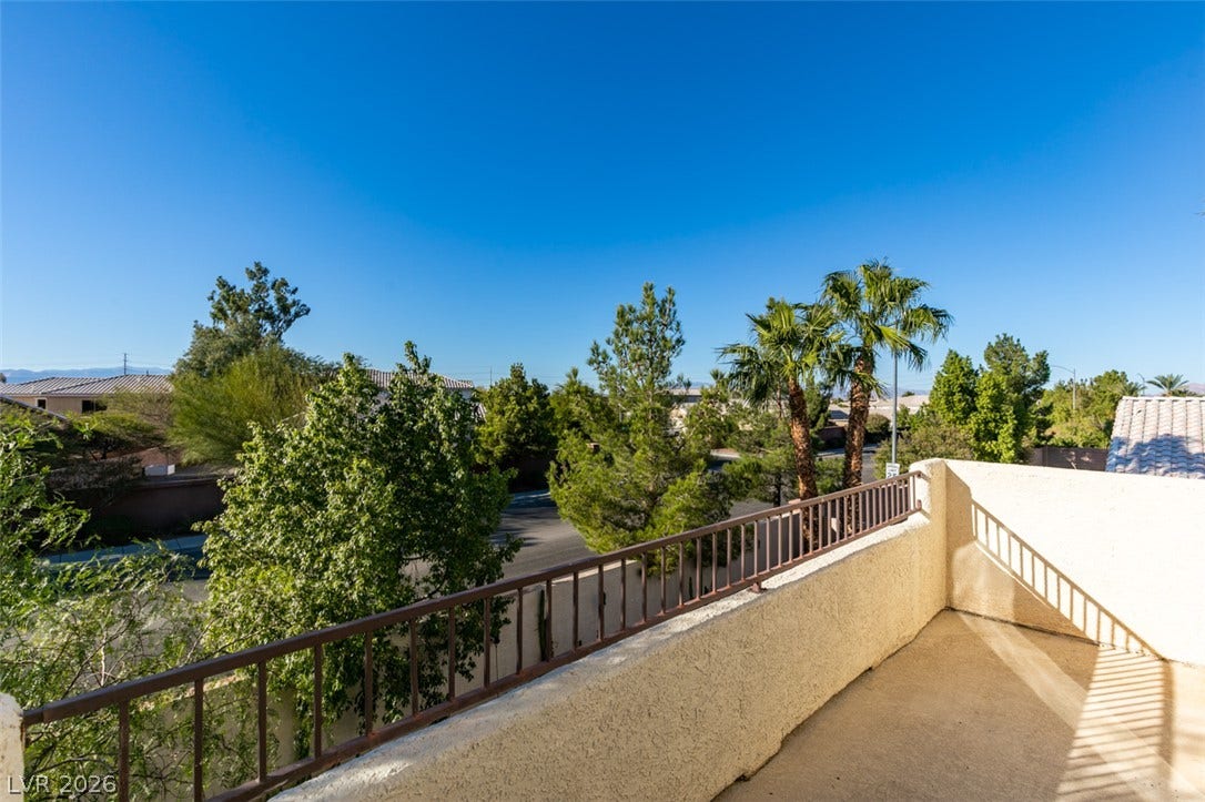 An elevated private balcony overlooks a lush neighborhood landscape under clear blue skies.