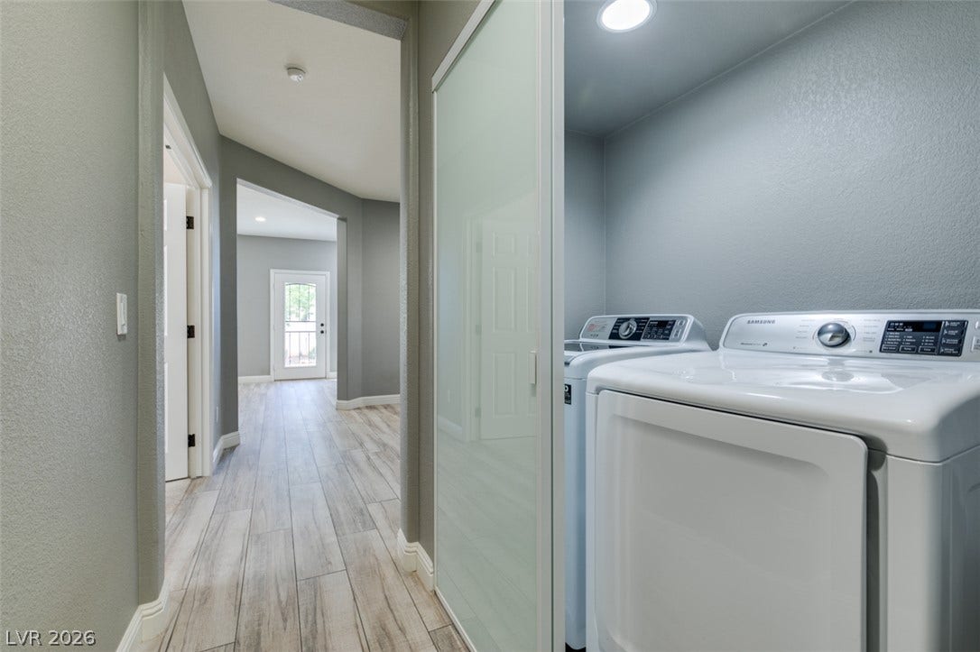 Modern sliding doors conceal a convenient laundry niche along a spacious wood-look tile hallway.