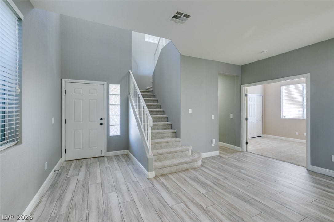 An inviting entryway opens to soaring ceilings, light-toned flooring, and a carpeted staircase.
