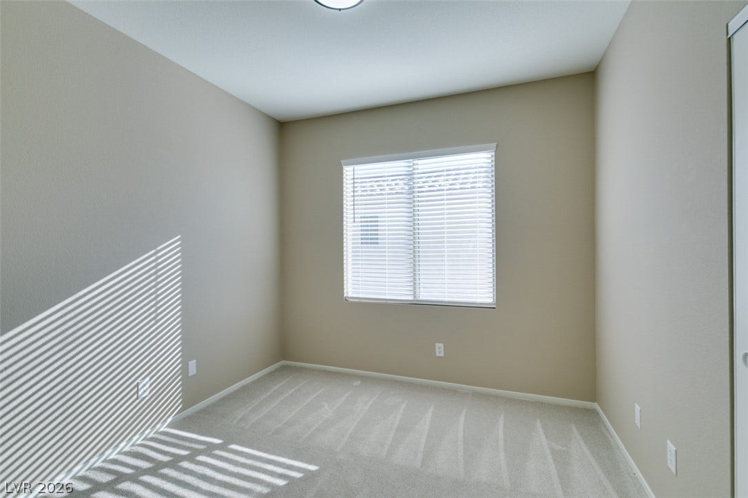 A window with horizontal blinds filters light across the neutral walls and carpeted flooring.