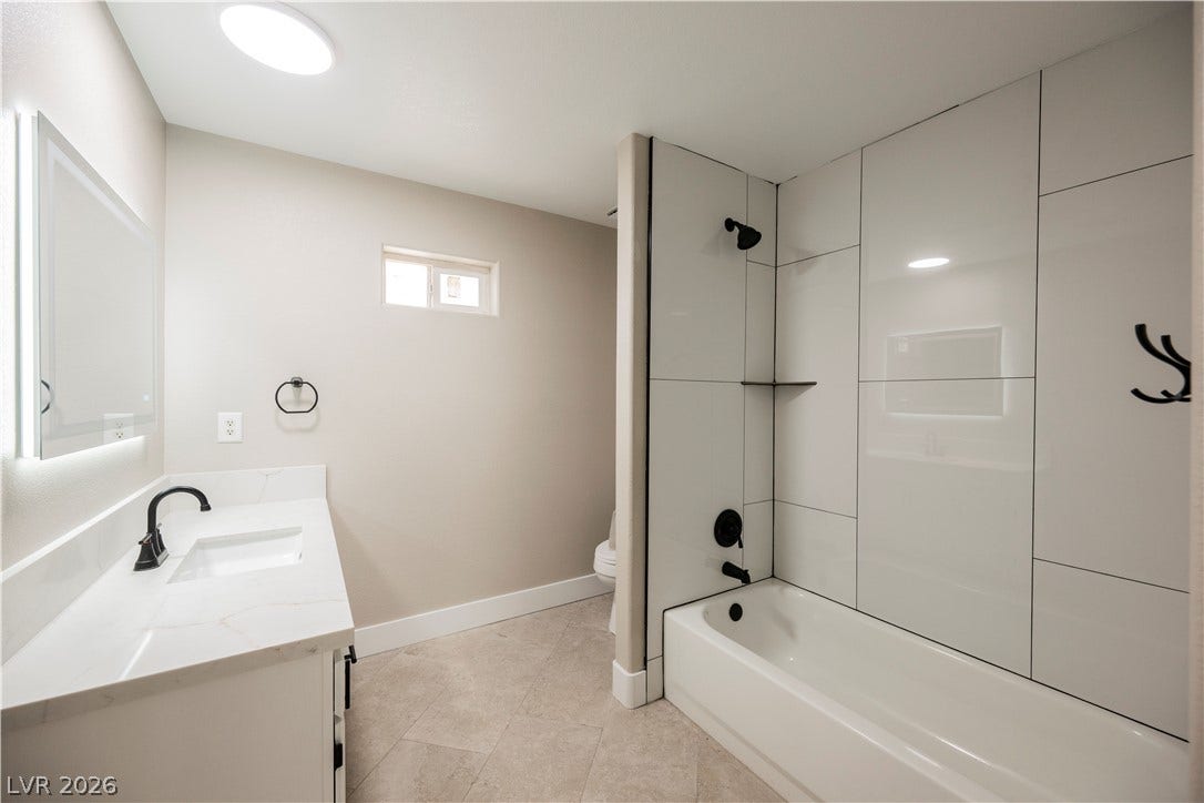 601 Sandy Drive, Henderson, NV 89002 Polished tile surrounds the bathtub in a cleanly designed bathroom featuring a modern vanity.