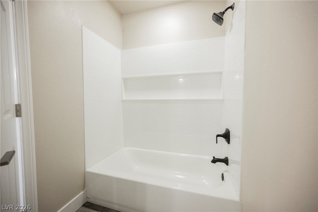 601 Sandy Drive, Henderson, NV 89002 A clean bathtub shower combination features white tile surrounds and dark hardware accents.