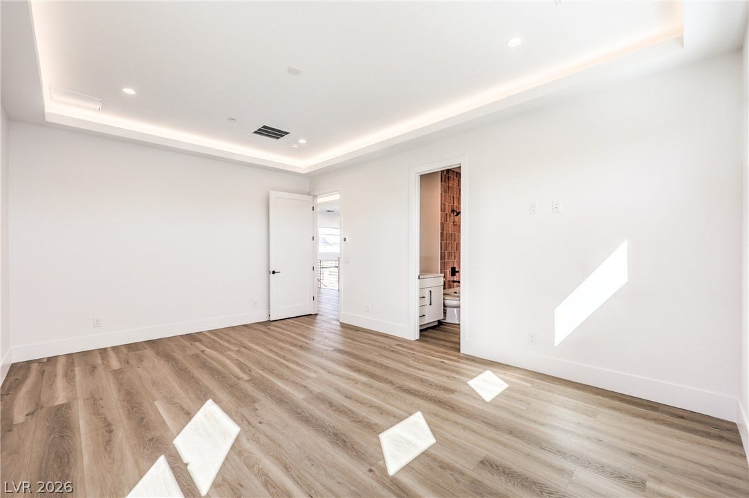 3051 E Serene Avenue, Henderson, NV 89074 Warm wood flooring and an elegant tray ceiling define this spacious modern bedroom.
