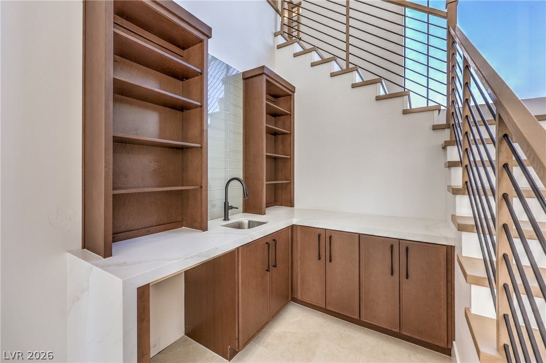 3051 E Serene Avenue, Henderson, NV 89074 Custom cabinetry and stone countertops elevate this functional wet bar beneath a floating staircase.