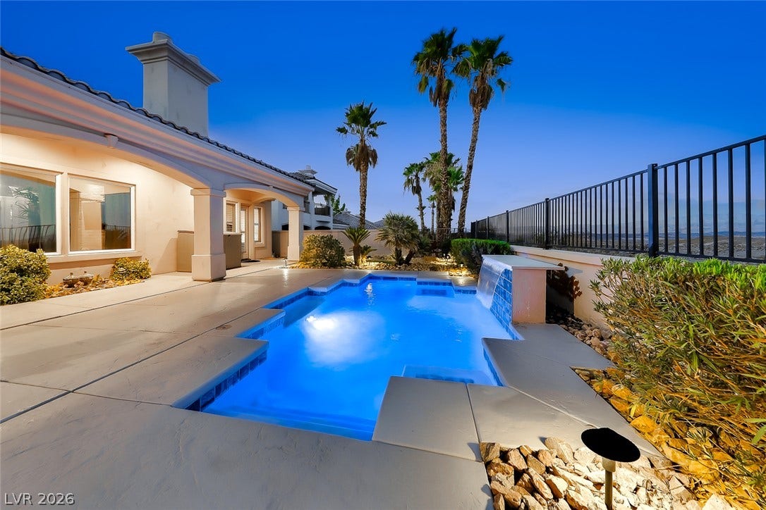 An inviting backyard oasis showcases a sparkling pool with water features framed by palm trees.