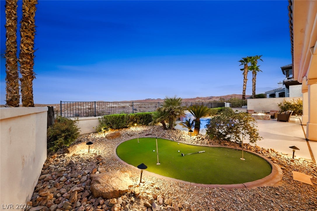 An inviting backyard putting green rests alongside a spacious patio with panoramic desert views.