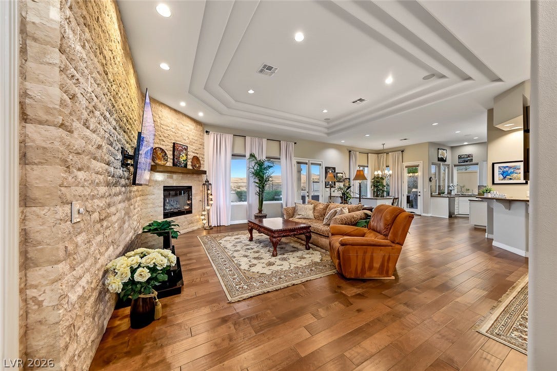 Rich hardwood floors complement the stacked-stone fireplace accent wall and multi-layered tray ceiling.