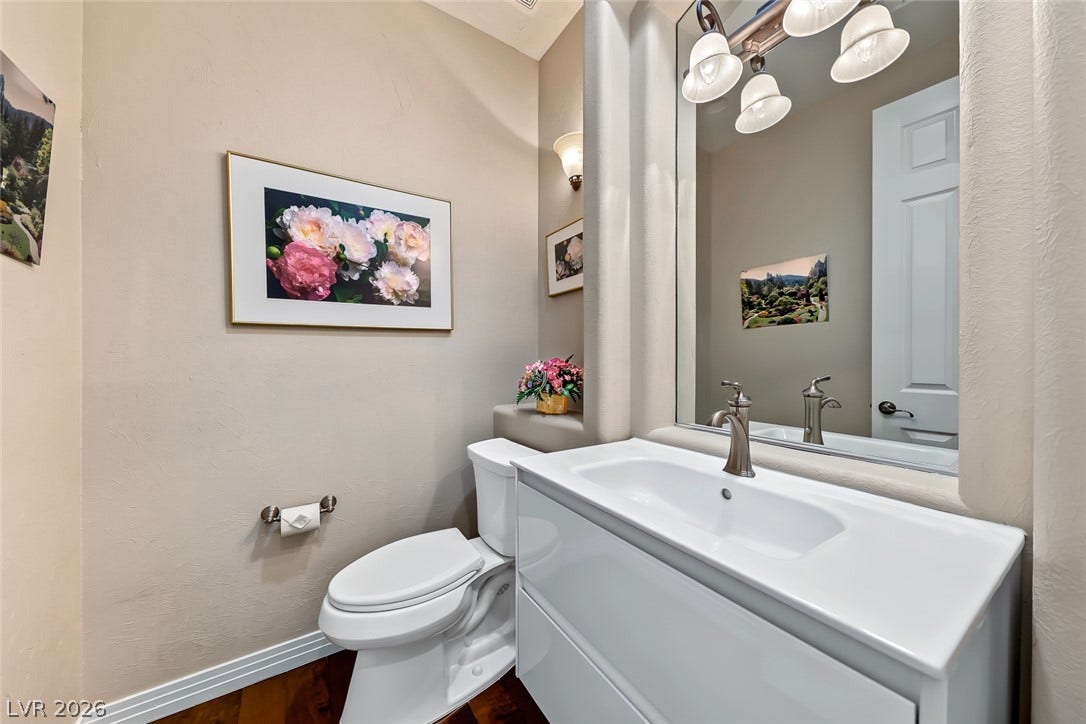Rich hardwood floors anchor this elegant powder room featuring a modern vanity and warm lighting.