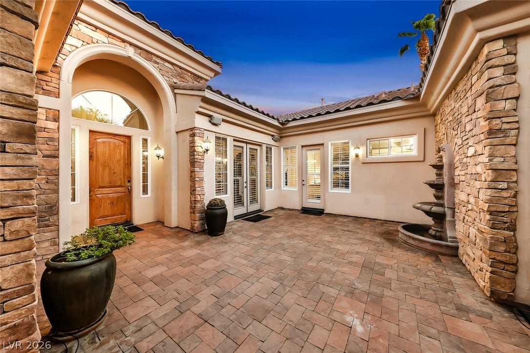 An inviting stone-clad courtyard features elegant pavers, a multi-tiered water fountain, and classic arched architectural details.