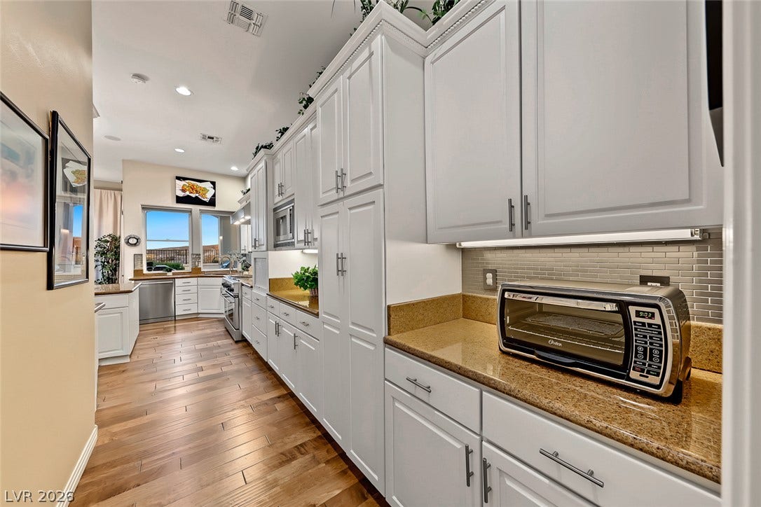 Rich hardwood flooring complements custom white cabinetry and stone countertops in this sleek galley kitchen.