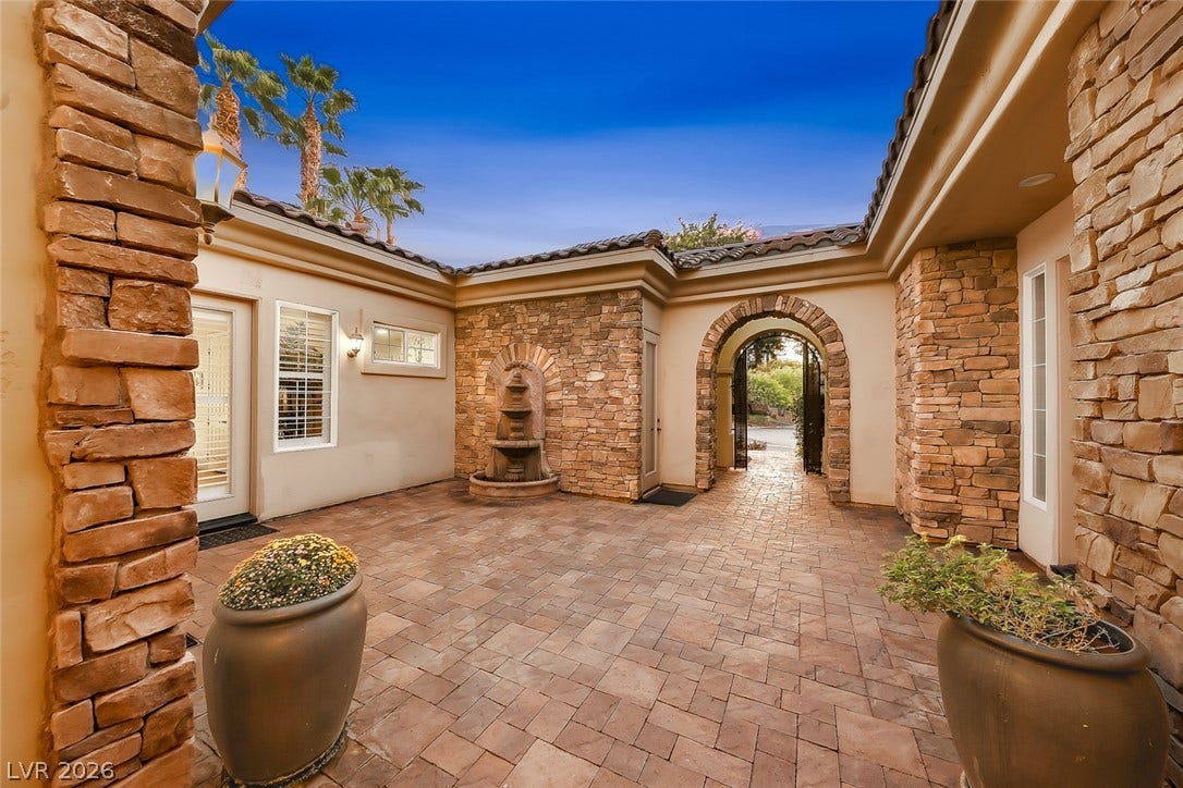 Stone pillars frame a beautifully paved courtyard complete with a multi-tiered fountain and arched entryway.