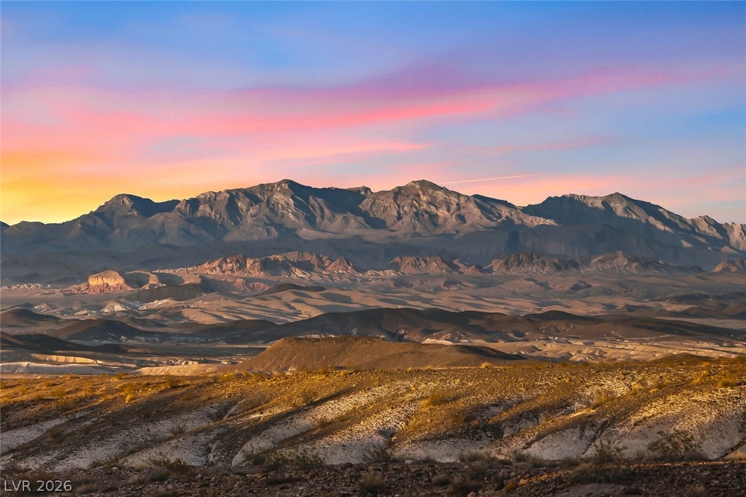Dramatic desert peaks rise beneath a vibrant twilight sky, showcasing rugged natural topography.