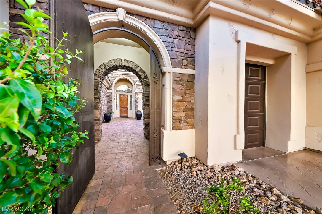 An arched entry gate opens to a beautifully paved courtyard flanked by stone accents.