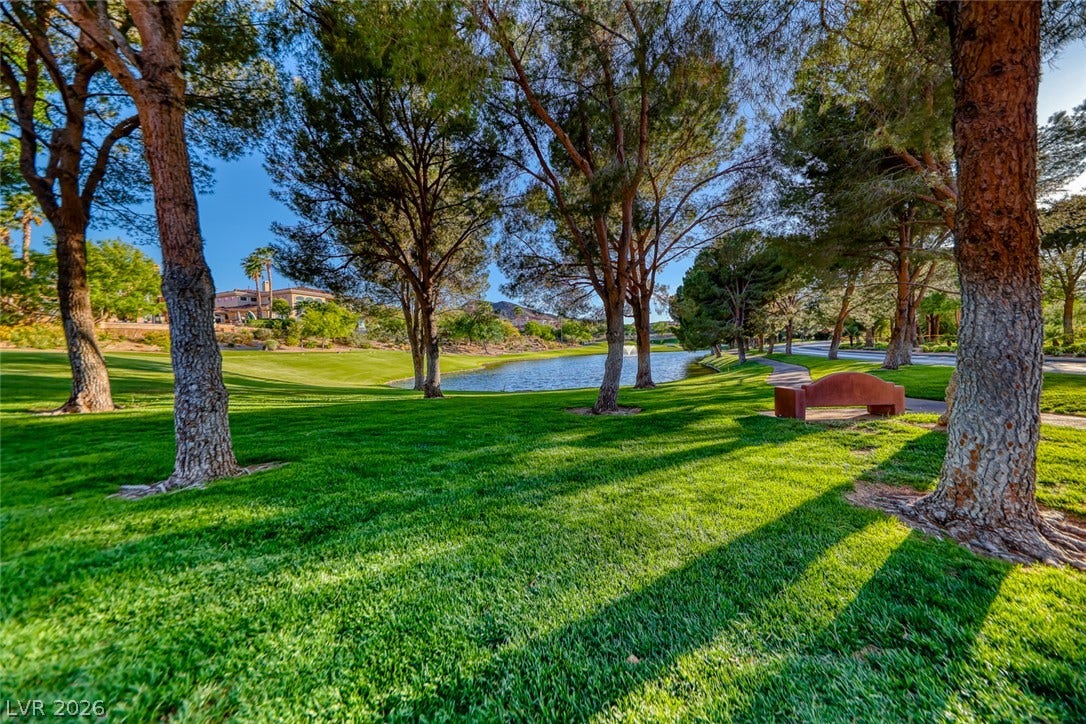 Mature trees shade a manicured green belt bordering a quiet pond.