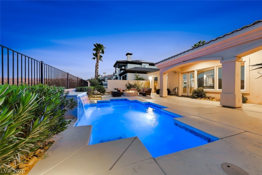 An inviting backyard oasis features a shimmering pool with integrated waterfall and concrete decking.