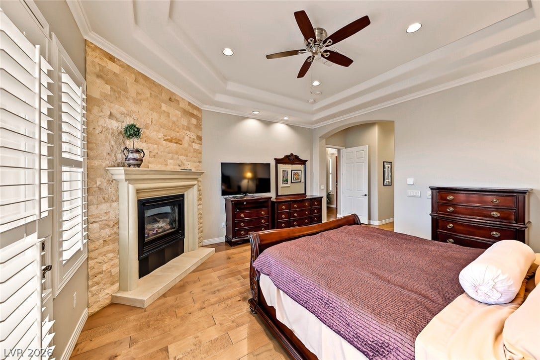 Rich hardwood floors complement a stone-clad fireplace and tiered tray ceiling in this spacious retreat.