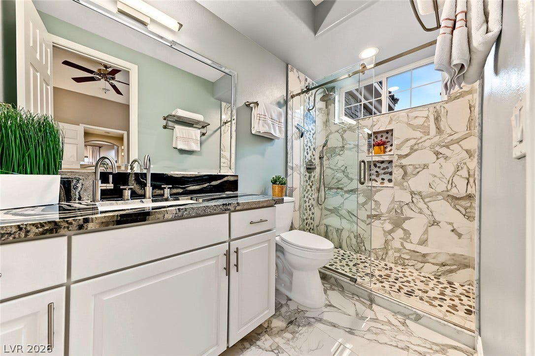 A glass-enclosed walk-in shower with stone tile highlights this modern primary bathroom.