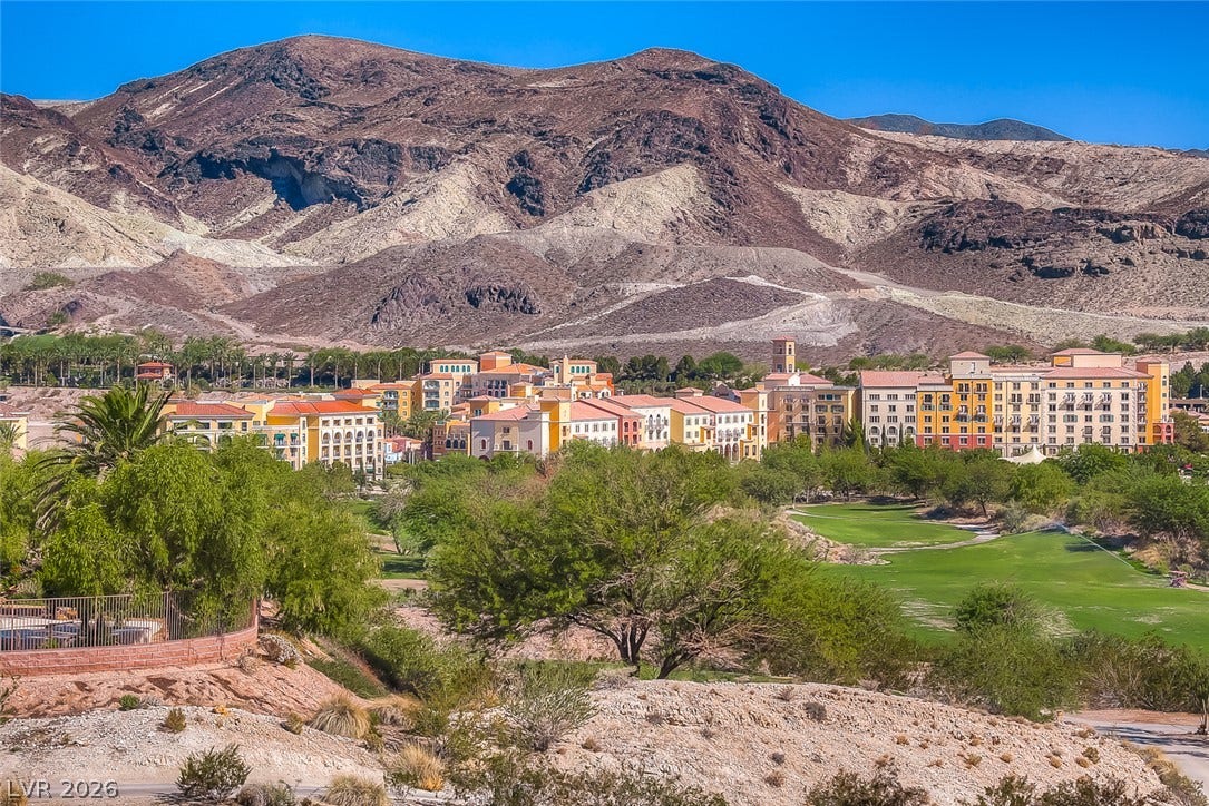 Dramatic mountain peaks rise sharply behind a lush golf course and vibrant hillside community.