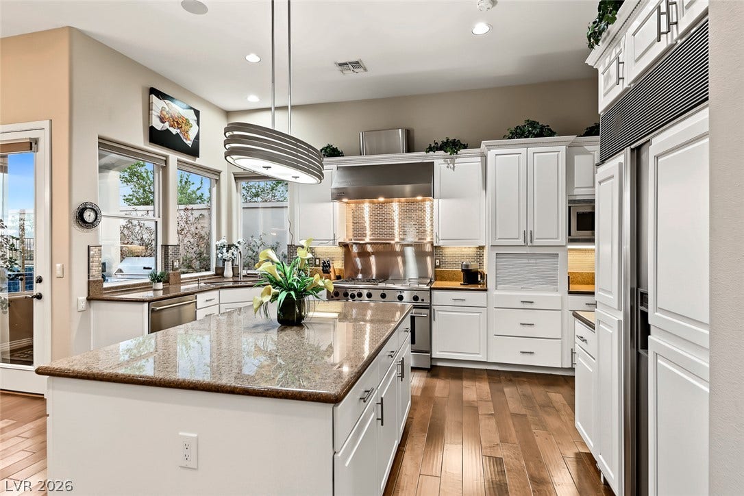 Polished granite countertops and classic white cabinetry define this kitchen space with hardwood flooring.