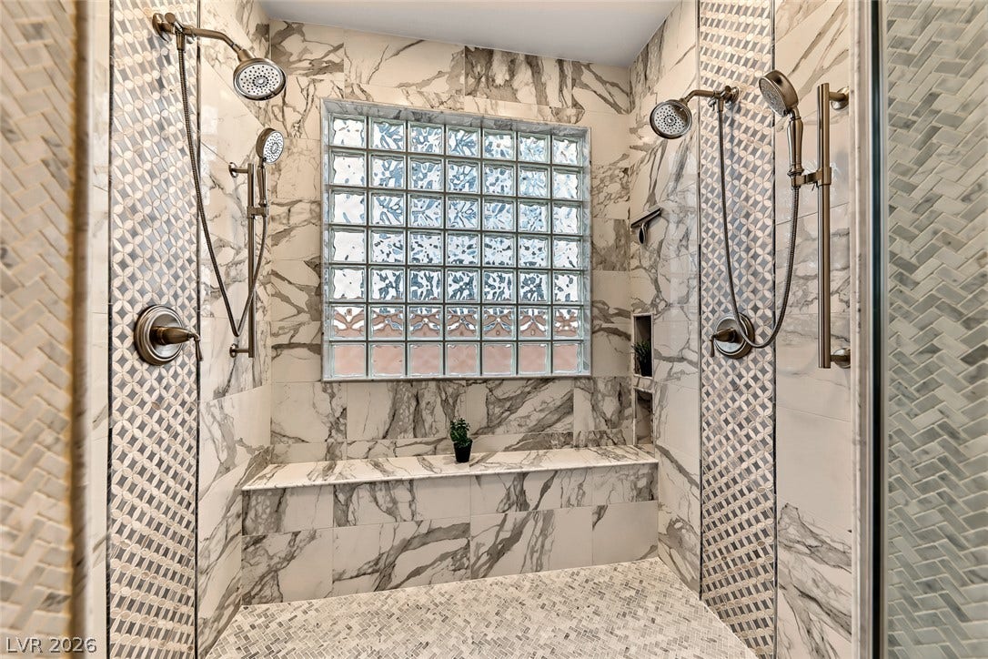 A spacious walk-in shower showcases elegant marble tiling and dual showerheads alongside a glass block window.