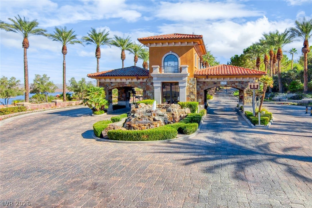 An elegant stone and stucco guard gate stands at the entrance under tile roofs.