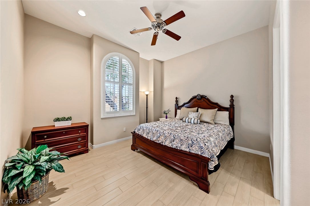 An arched window with plantation shutters accents this bedroom featuring high ceilings and light flooring.