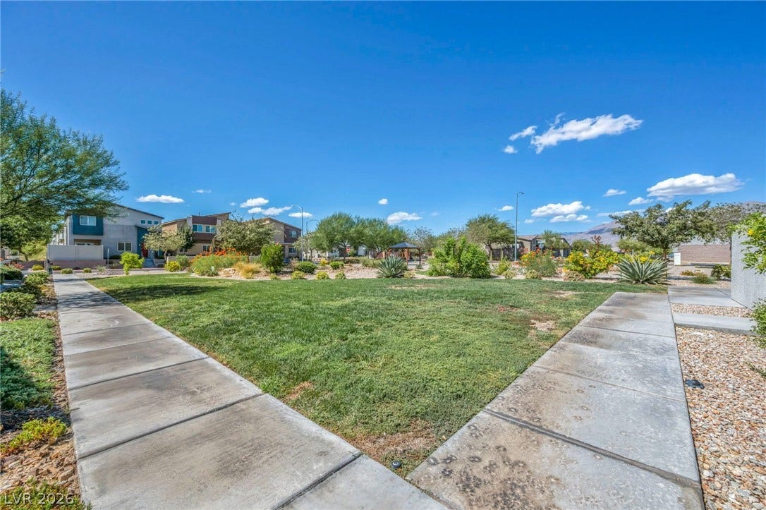 7481 Garnet Moon Street, North Las Vegas, NV 89084 Concrete walkways border a manicured green lawn under clear blue skies.