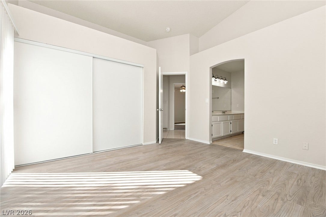 4448 Ryder Lane, North Las Vegas, NV 89031 Vaulted ceilings and wood-style flooring elevate this modern bedroom with an attached bath.