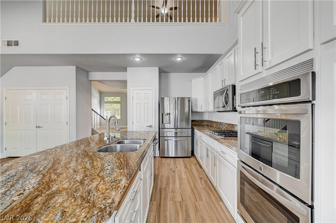 8908 Sheep Ranch Court, Las Vegas, NV 89143 High ceilings and warm wood-look flooring complement the expansive granite countertops in this kitchen.