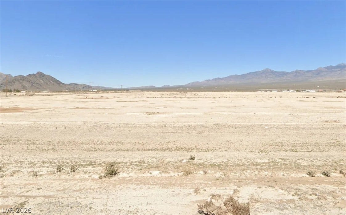 A vast level terrain stretches toward a dramatic mountain range under clear blue skies.